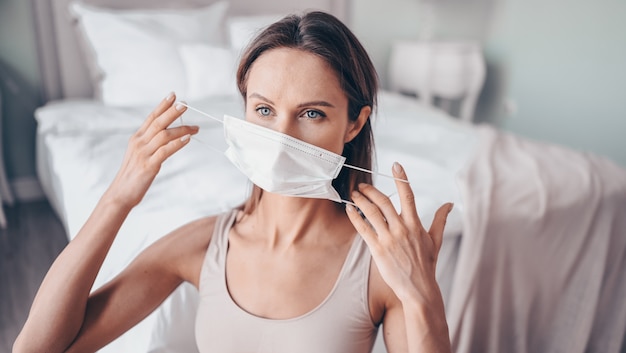 home fitness. young fit slim woman in protection face mask doing morning work-out yoga exercises in bedroom