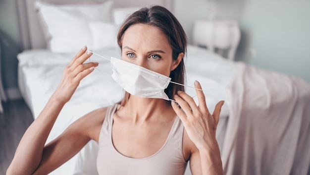 Home fitness. Young fit slim woman in protection face mask doing morning work-out yoga exercises in bedroom