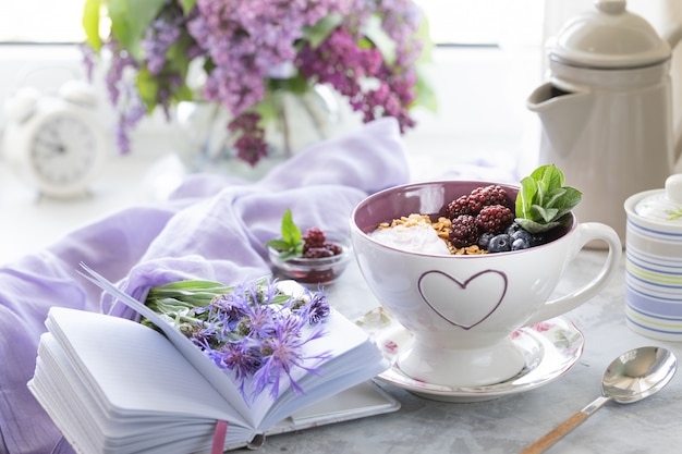 Home granola with berries on the table near the window with a bouquet of lilacs.