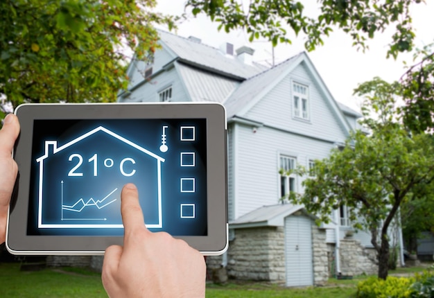 home, housing, people and technology concept - close up of man hands pointing finger to tablet pc computer and regulating room temperature over house background