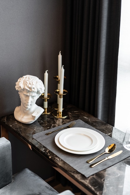 Foto interno di casa con tavola della sala da pranzo con stoviglie e posate in acciaio inossidabile dorato su piano in marmo. interior design