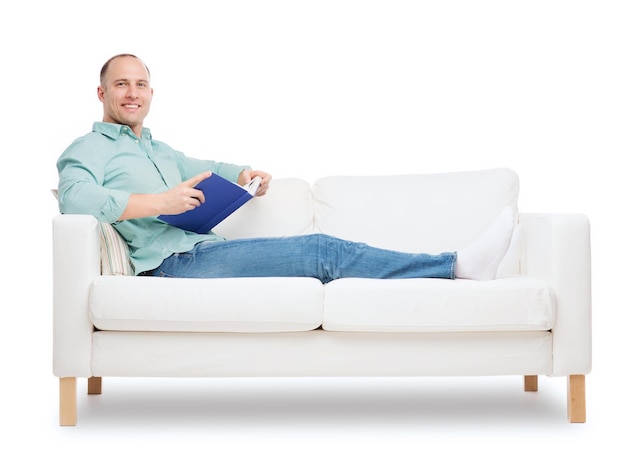 home, leisure and happiness concept - smiling man lying on sofa with book