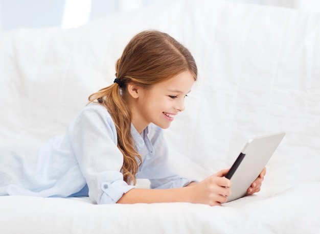 home, leisure, new technology and music concept - smiling little girl with tablet pc computer and headphones at home