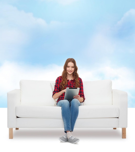 концепция дома, отдыха, технологий и счастья - улыбающаяся девочка-подросток, сидящая на диване с планшетным компьютером