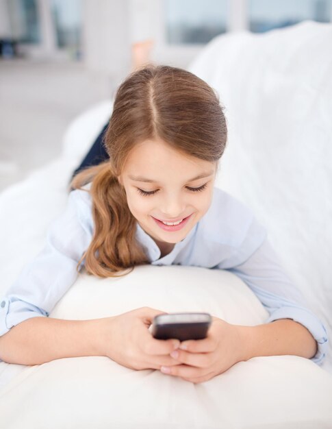 home, leisure, technology and internet concept - little student girl with smartphone at home