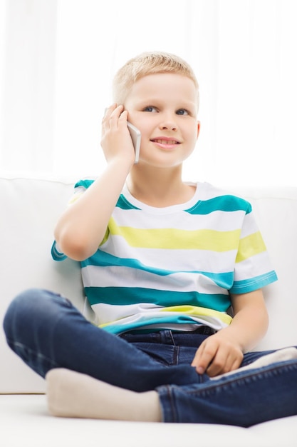 home, leisure, technology and internet concept - smiling little boy with smartphone at home