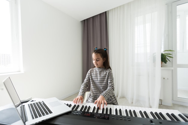 ピアノに寄る少女のための音楽のホームレッスン。検疫中の自宅での子供のための活動のアイデア。音楽のコンセプト