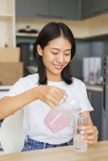 Home lifestyle concept Jonge vrouw giet water uit de kruik in glas terwijl ze thuis een snack heeft