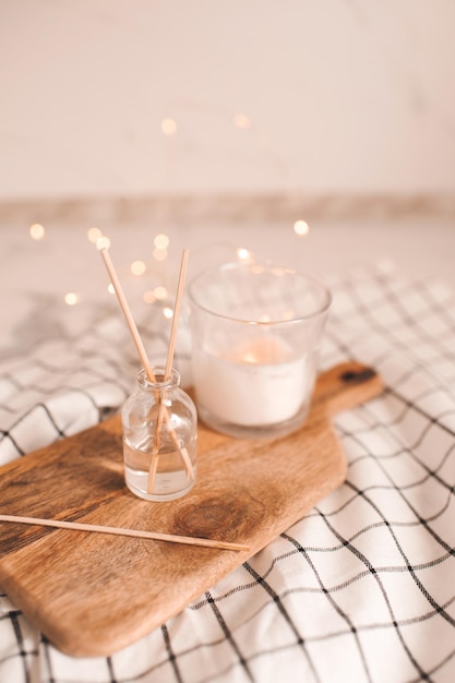 Home liquid fragrance in glass bottle with wooden bamboo sticks and scented candle on tray over glow lights closeup. Home decor. Warm cozy atmosphere.