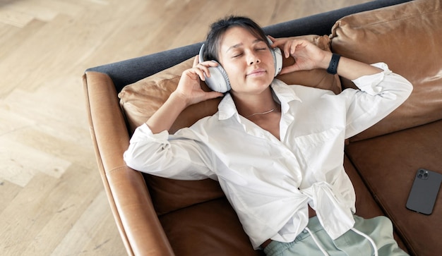 Дома слушая плейлист музыки в наушниках в приложении аудиокнига женщина отдыхает