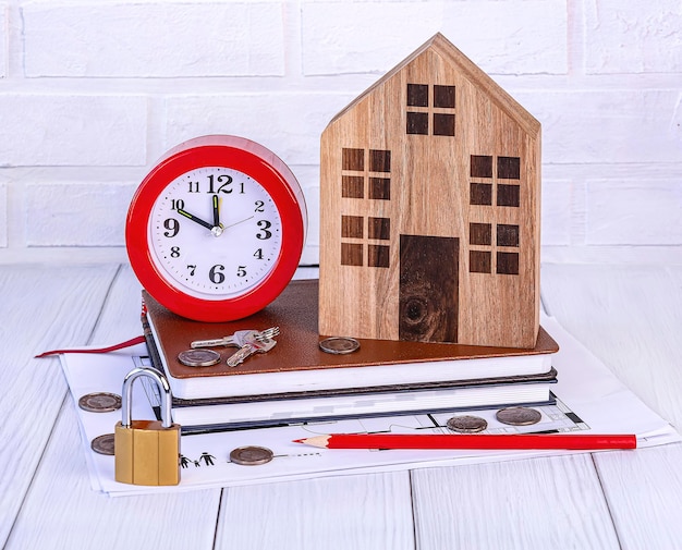 Photo home loan concept wooden house red alarm clock house keys coins stationery on white background