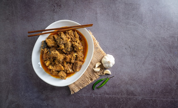 home made beef curry in white bowl with chopstick and salt garlic cloves chillies top view 