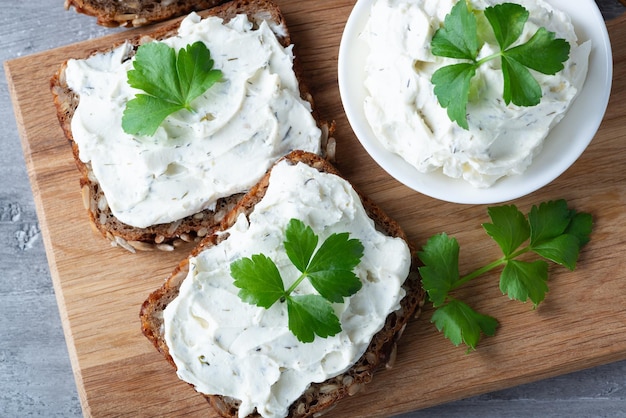 Home made bread on a wooden cutting board with curd cheese and ricotta and herbs Decorated with green herbs