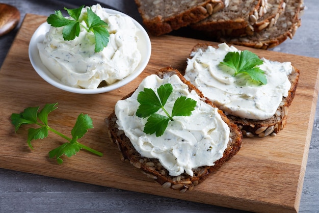 Home made bread on a wooden cutting board with curd cheese and ricotta and herbs