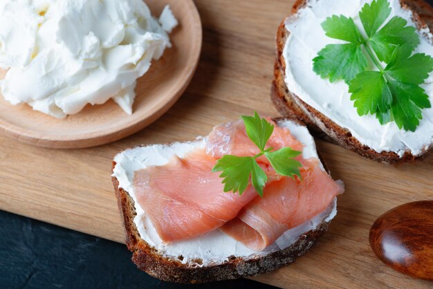 Home made bread on a wooden cutting board with curd cheese and salmon Decorated with green herbs