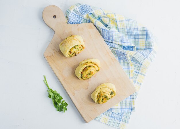 Panini fatti in casa con aglio, prezzemolo verde e peperone dolce in un tovagliolo e tagliere di legno bianco.