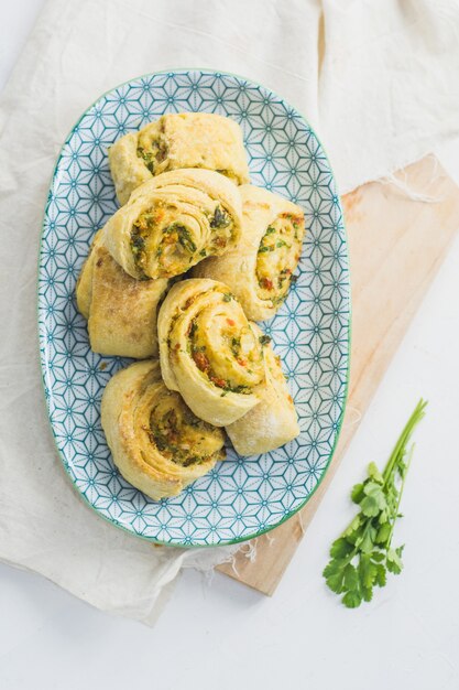 Home made buns with garlic, green parsley and sweet pepper in a plate with napkin and wooden cutting board white.