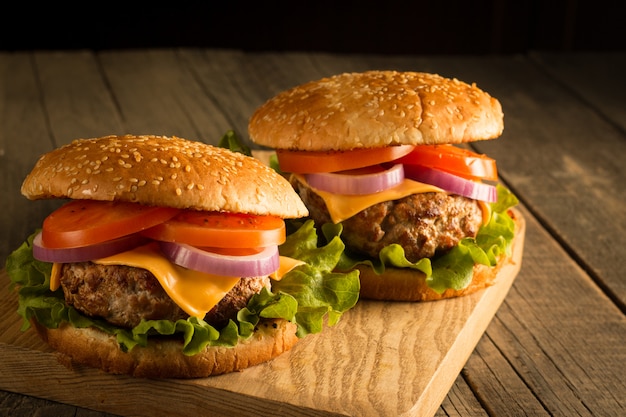 Home made hamburger with beef, onion, tomato, lettuce and cheese. Fresh burger close up on wooden rustic table with potato fries, beer and chips. Cheeseburger.