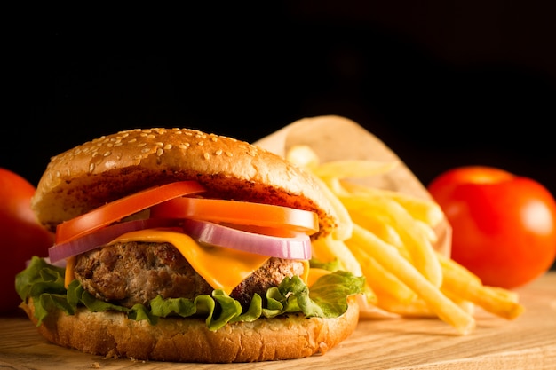 Home made hamburger with beef, onion, tomato, lettuce and cheese. Fresh burger close up on wooden rustic table with potato fries, beer and chips. Cheeseburger.