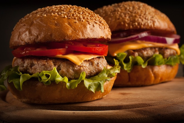 Home made hamburger with beef, onion, tomato, lettuce and cheese. Fresh burger close up on wooden rustic table with potato fries, beer and chips. Cheeseburger.