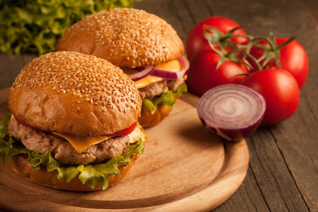 Hamburger fatto in casa con carne di manzo, cipolla, pomodoro, lattuga e formaggio. fine fresca dell'hamburger su sulla tavola rustica di legno con le patate fritte, la birra e le patatine fritte. cheeseburger.