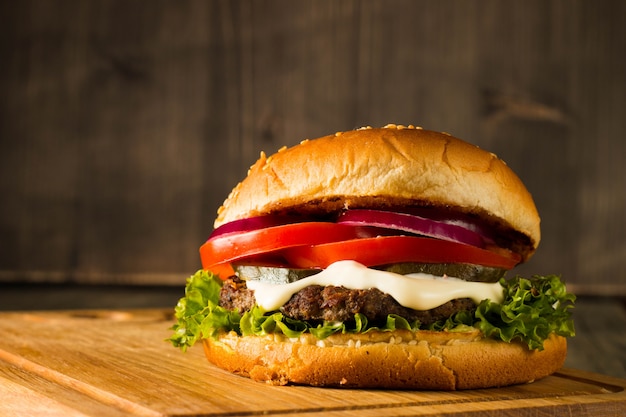 Home made hamburger with beef, onion, tomato, lettuce and cheese. Fresh burger close up on wooden rustic table with potato fries, beer and chips. Cheeseburger.