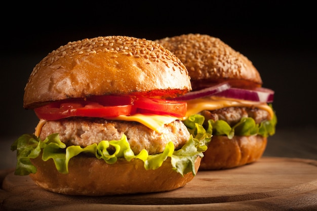 Home made hamburger with beef, onion, tomato, lettuce and cheese. Fresh burger close up on wooden rustic table with potato fries, beer and chips. Cheeseburger.