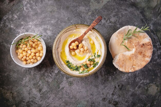 Home made hummus bowl, decorated with boiled chickpeas, herbs, pita and olive oil over a rustic metal background. Top View.