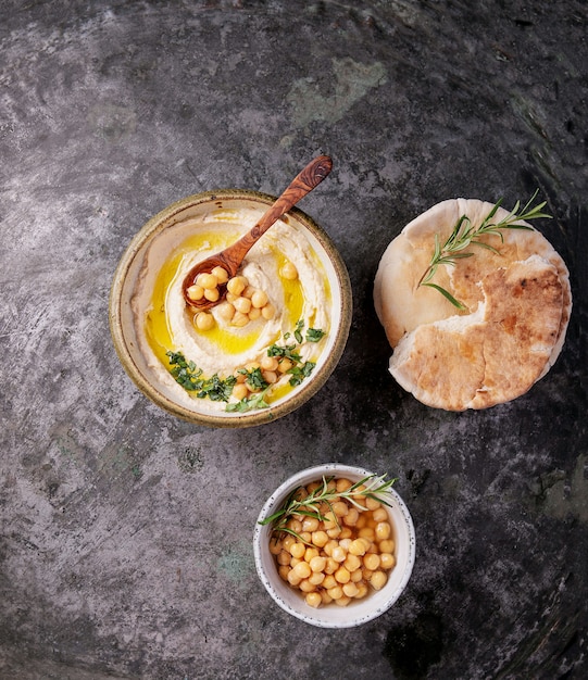 Home made hummus bowl, decorated with boiled chickpeas, herbs, pita and olive oil over a rustic metal background. Top View.