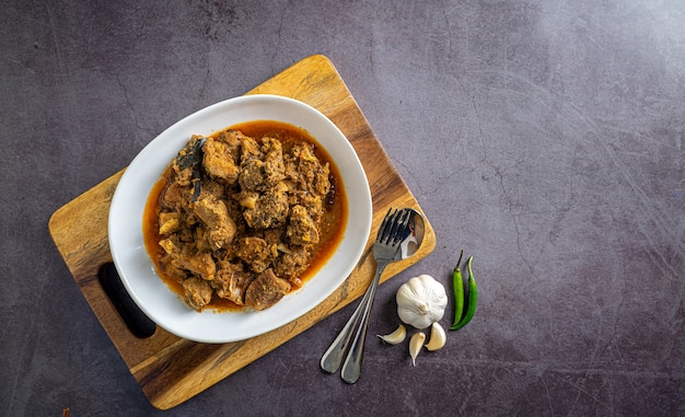 Photo home made spicy beef curry in white bowl with spoon set and spices on wooden tray top view