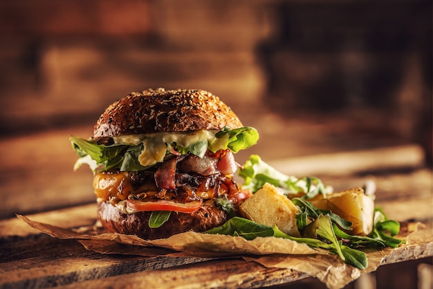 Photo home made tasty burger with bacon onion cheese ane lettuce on wooden box.