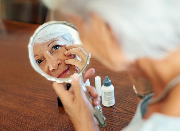 Home mirror and mature woman for skincare checking and face inspection with hand gesture Reflection elderly person and beauty treatment for wrinkles anti aging and skin texture in house
