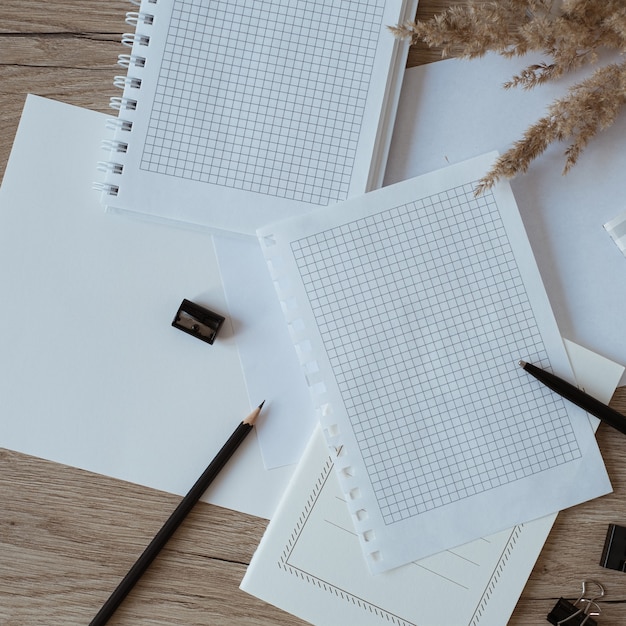 home office desk workspace with blank paper sheets, notebook, pampas grass