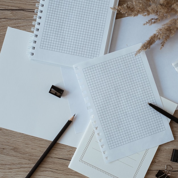 Home office desk workspace with blank paper sheets, notebook, pampas grass