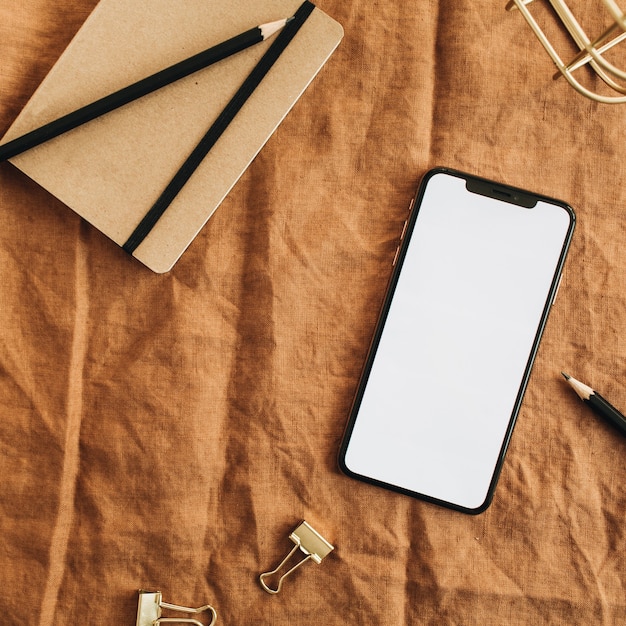 Home office desk workspace with blank screen smart phone on brown blanket. Flat lay, top view minimal blog hero header.