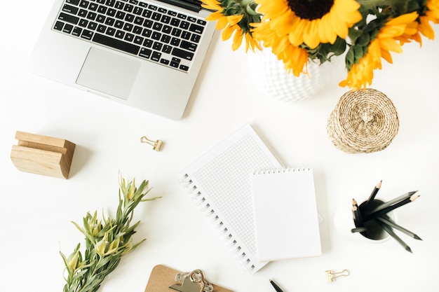 Home office desk workspace with laptop, notebook, clipboard, yellow sunflowers bouquet on white