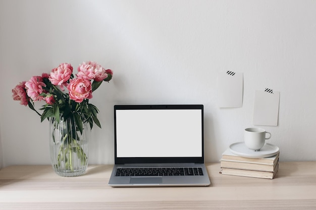 Home office still life scene notebook computer and memo cards\
mockups vase with pink peonies flowers books and cup of coffee\
wooden table elegant feminine working space living room\
interior