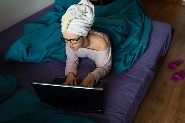 Quarantena di isolamento per il telelavoro dell'ufficio domestico una giovane ragazza che lavora su un laptop seduto su un letto a casa in un asciugamano dopo la doccia