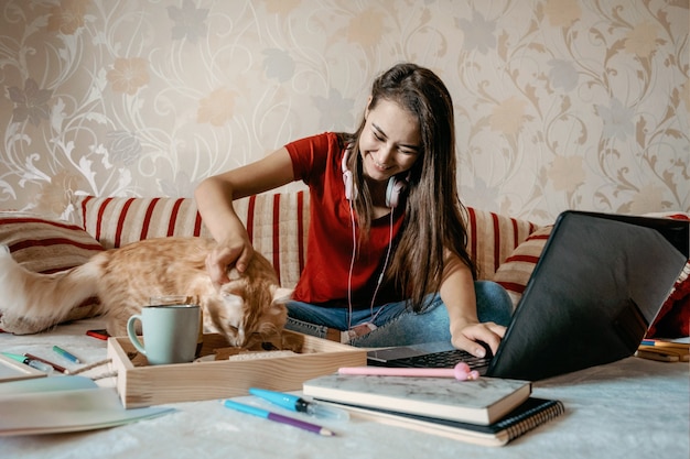 홈 오피스 작업 공간은 노트북과 고양이가 소파에서 일하는 가정 개념의 젊은 여성에서 일합니다.