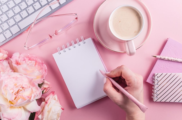 Home office workspace - modern keyboard, cup of coffee and fresh rose flowers on pink background.