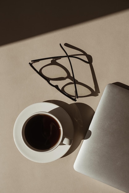 Photo home office workspace with laptop computer coffee cup glasses in sunlight shadows flatlay top view aesthetic luxury bohemian minimal lady boss business lifestyle concept