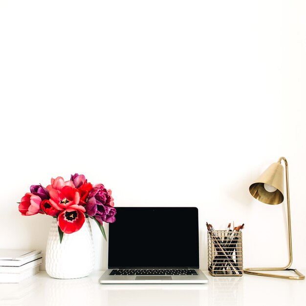 Home office workspace with laptop, tulip flowers bouquet, stationery, lamp