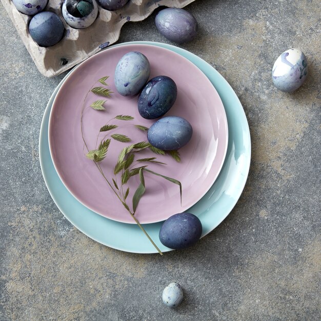 Домашние крашеные яйца на тарелке с листьями и лоток для бумаги на бетонном фоне