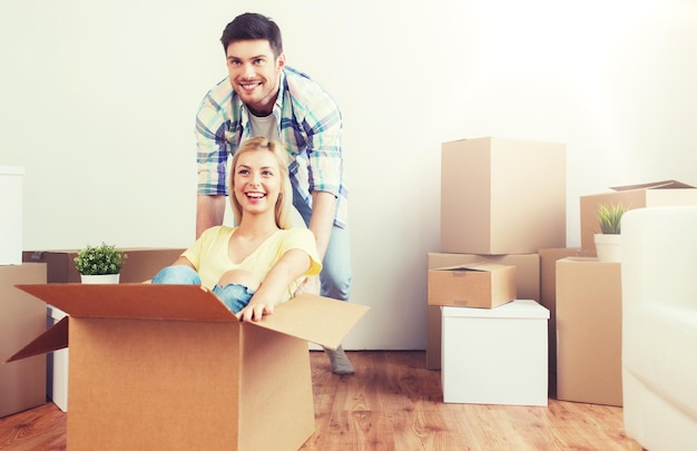 home, people, moving and real estate concept - happy couple having fun and riding in cardboard boxes at new home