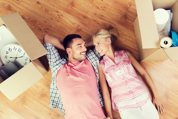 home, people, repair and real estate concept - happy couple with cardboard boxes and stuff lying on floor to new place