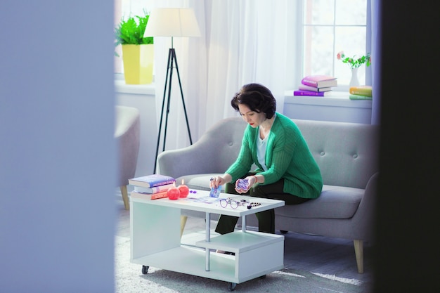 At home. Pleasant dark haired woman sitting on the sofa while using tarot cards