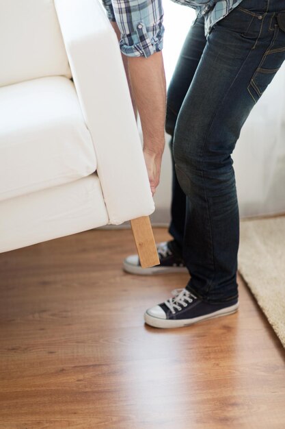 home, real estate and furniture concept - close up of male lifting up sofa to move