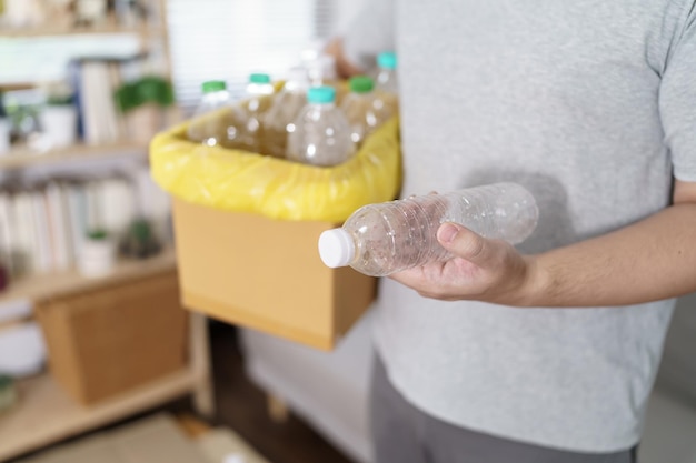 写真 ホームリサイクルエコグリーンゼロコンセプト 家で黄色いゴミ袋で空のプラスチックボトルをリサイクルビンに捨てる男