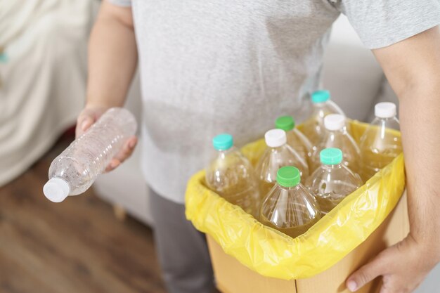 Foto home recycle eco green zero concept uomo che lancia una bottiglia di plastica vuota nel cestino per il riciclaggio con sacchi di immondizia gialli a casa