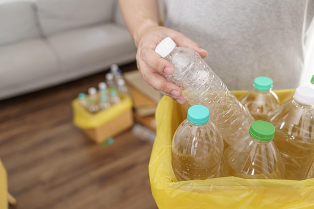 ホームリサイクルエコグリーンゼロコンセプト自宅で黄色のゴミ袋を持つリサイクル箱に空のペットボトルを投げる男性